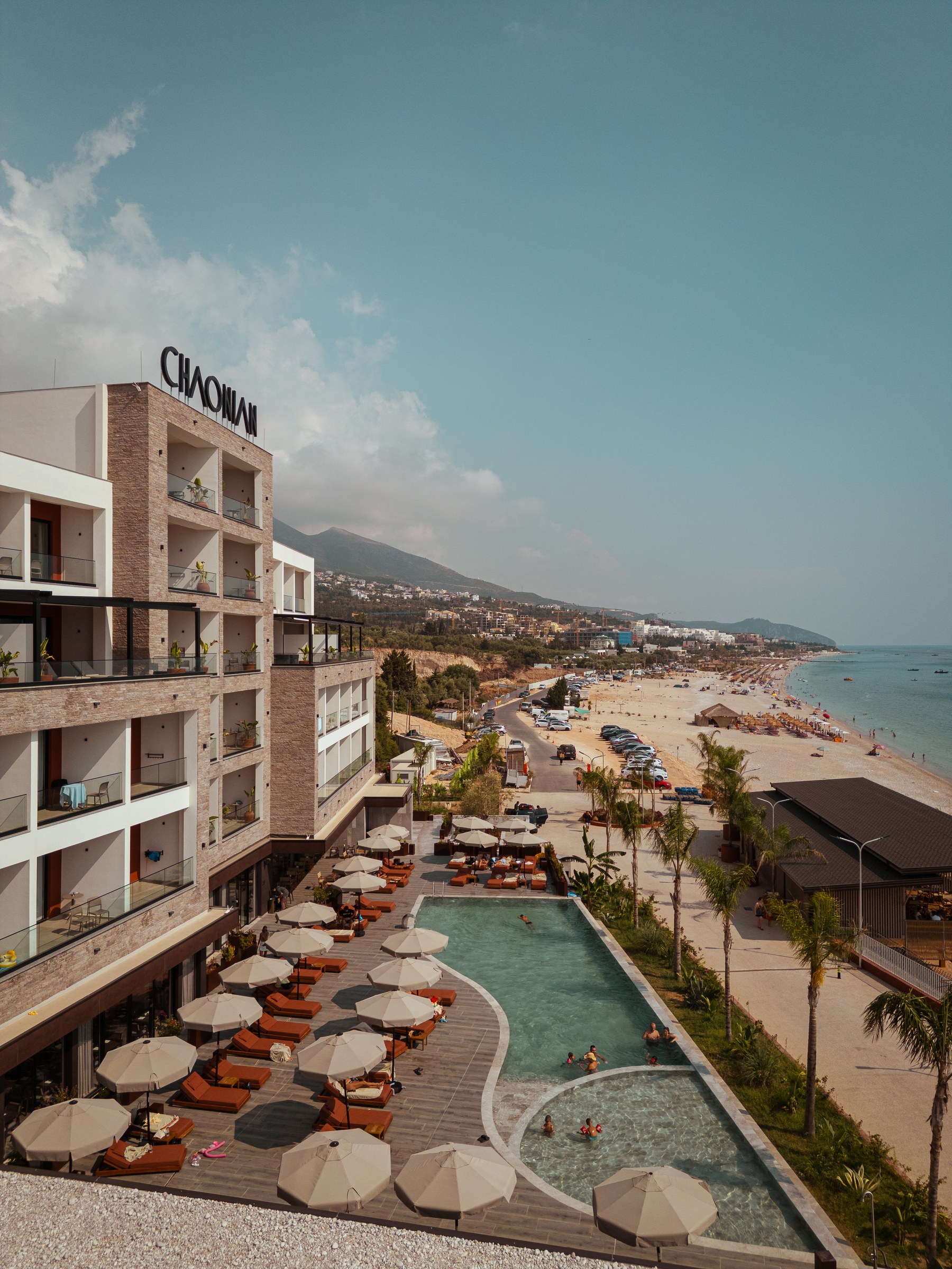 Chaonian Hotel from the air — the facade under the CHAONIAN sign, the pool terrace and Drymades beach running up the coast
