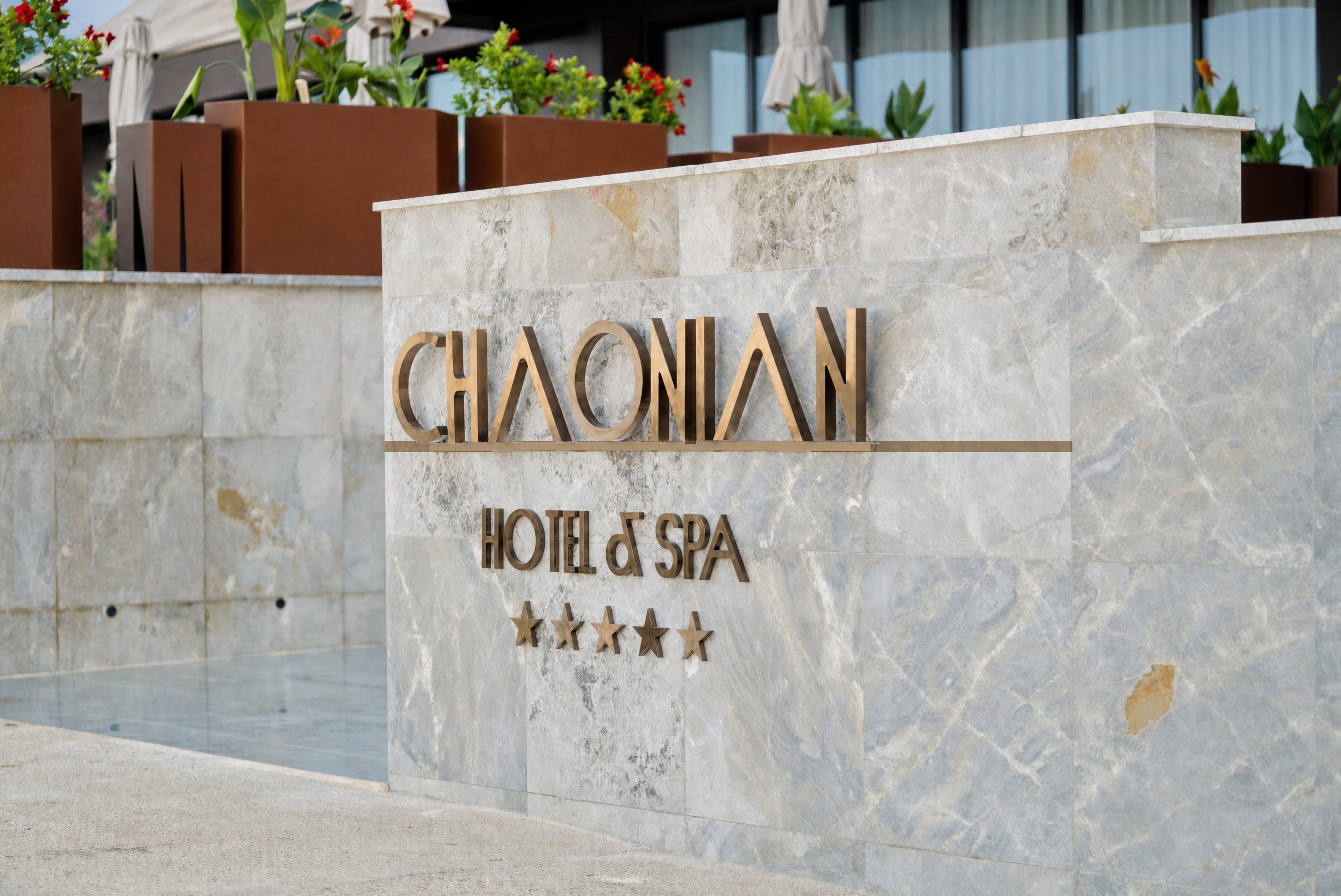 Chaonian Hotel — shkrimi prej bronzi në murin prej mermeri të hyrjes