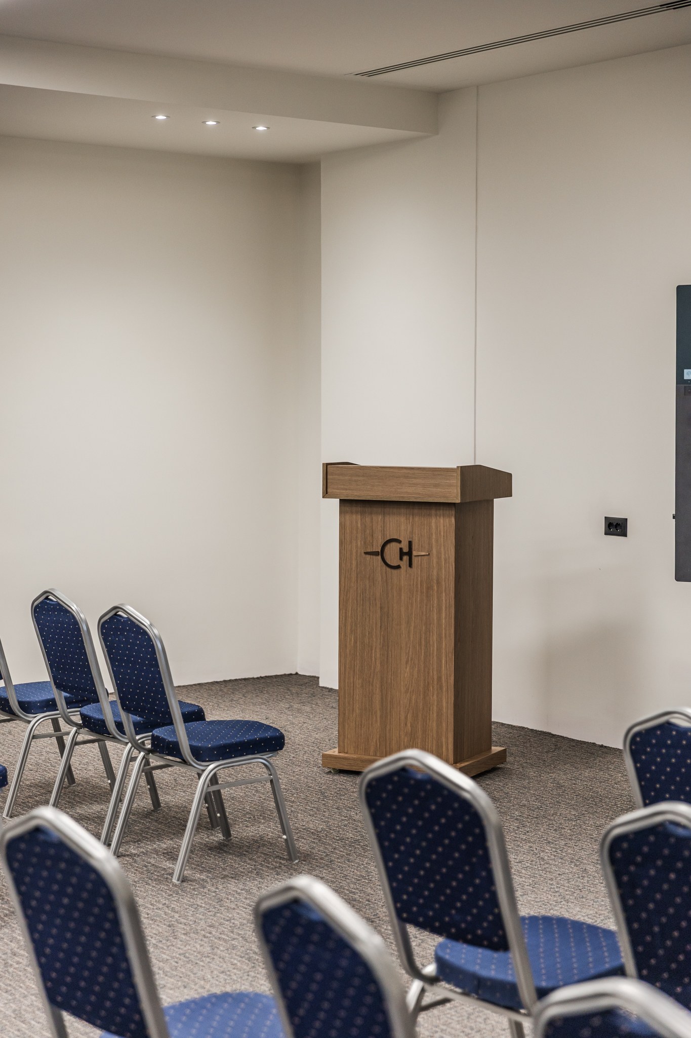 Chaonian's conference hall — the oak lectern with the CH monogram, rows of banquet chairs before it
