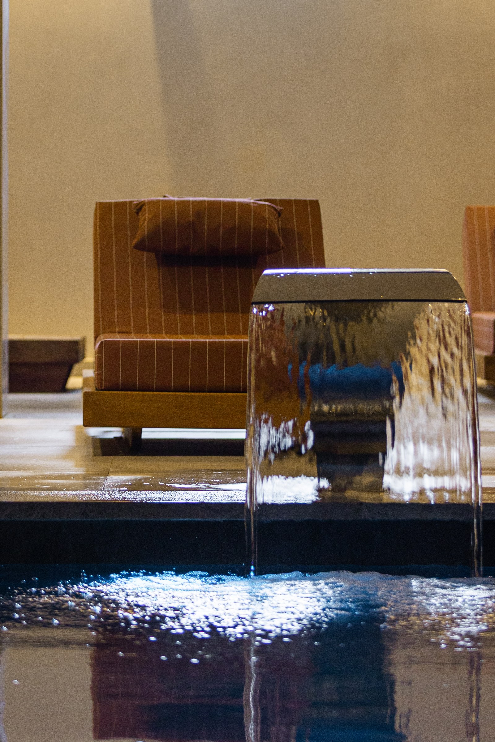 The Chaonian Spa pool hall — a steel water spout pouring into the heated pool, loungers behind