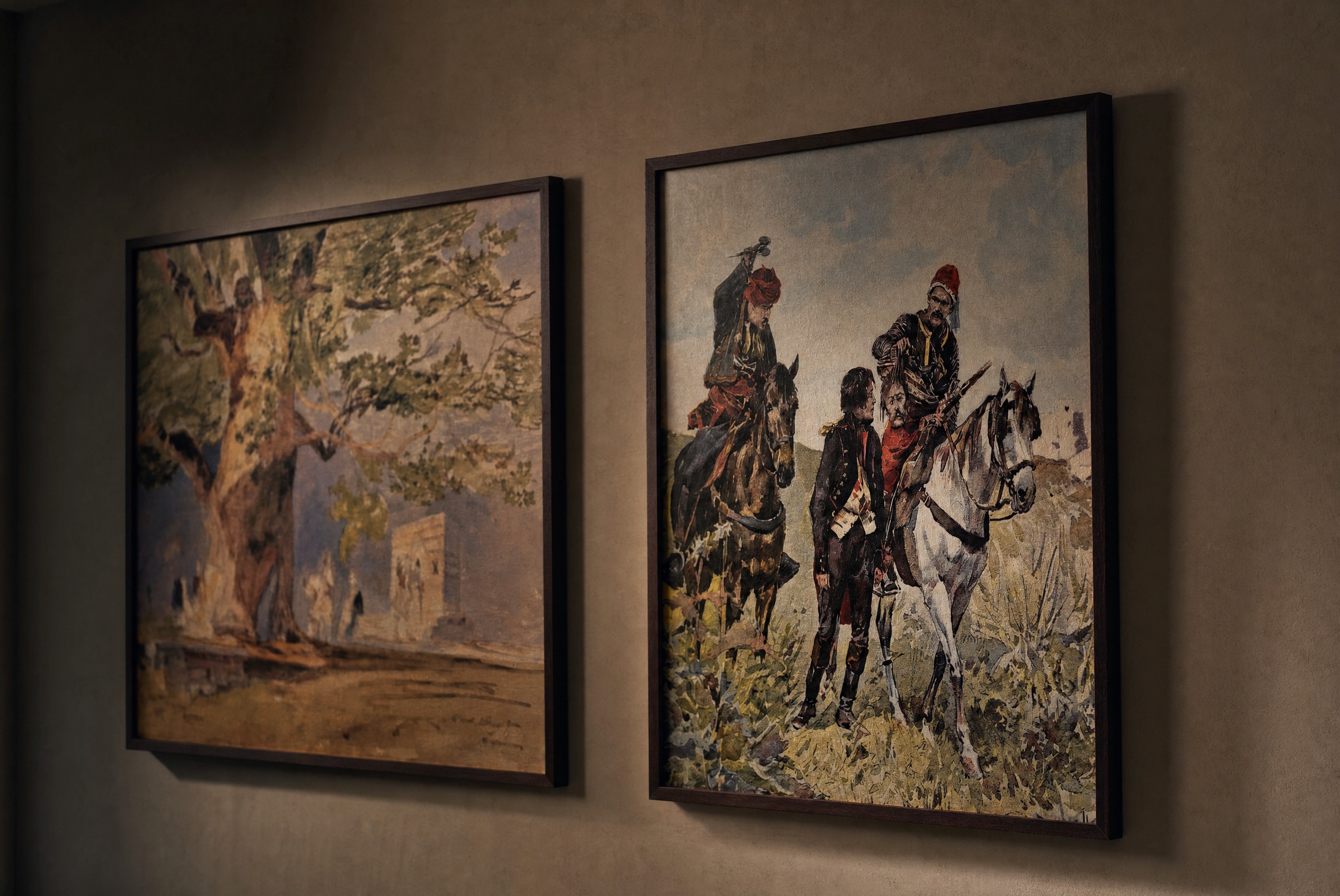 Two framed paintings at Chaonian — an ancient Albanian plane tree and horsemen in traditional dress — on a warm-lit wall