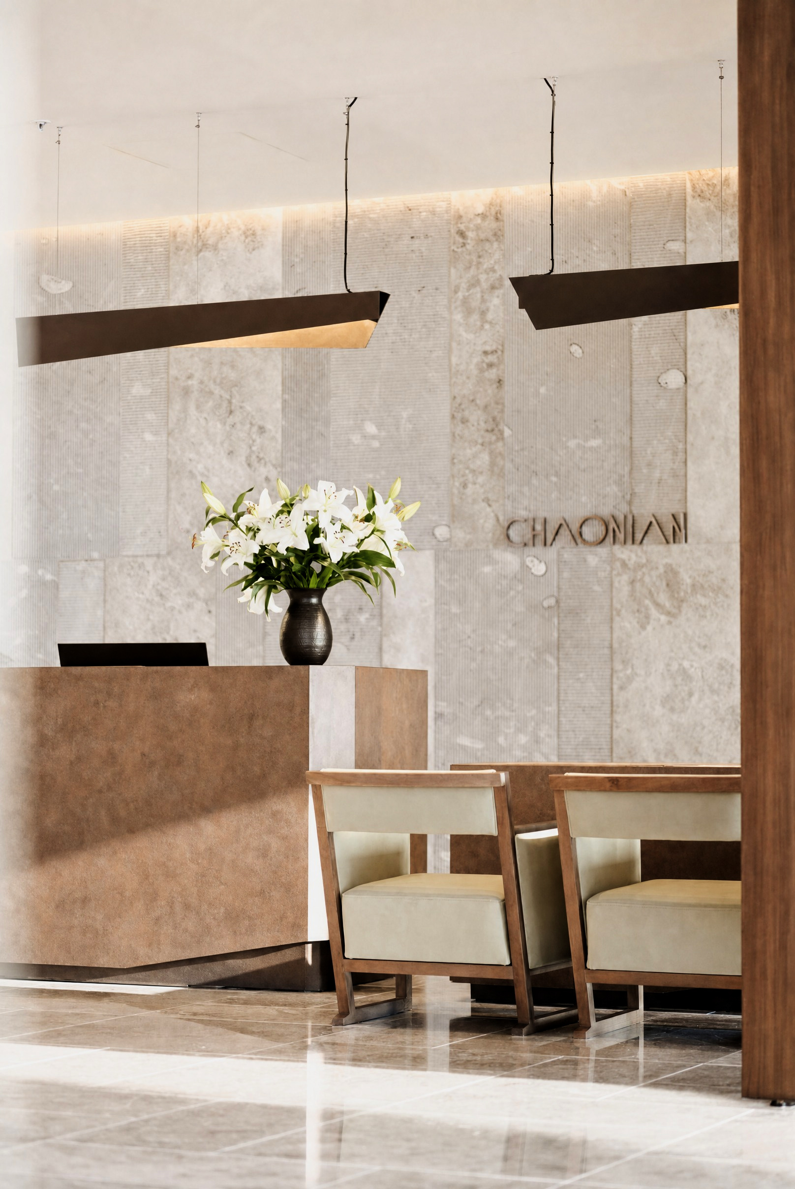The reception desk beneath bronze lettering on fluted travertine, dressed with white lilies
